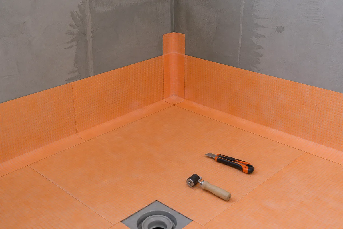 Natte d&rsquo;étanchéité souple collée sur un sol de douche avec bande d&rsquo;angle en attente de carrelage
