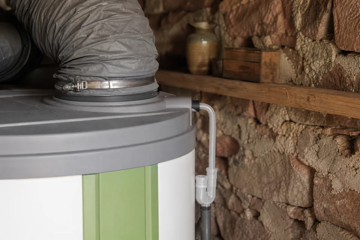 Ballon thermodynamique installé dans un cellier non chauffé aux murs de pierre calcaire, gaine d&rsquo;air et raccordements cuivre visibles