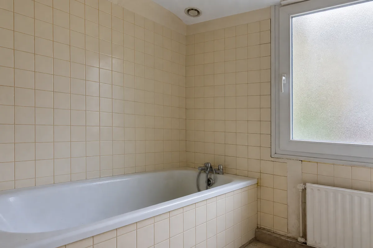 Salle de bains pavillonnaire des années 1980 avant rénovation, baignoire encastrée et faïence murale claire